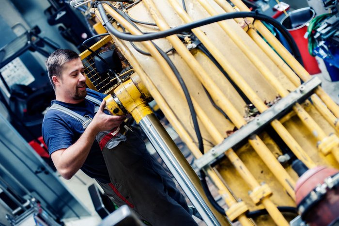 Servicearbeit an Hydrauliksystem Mitarbeiter überprüft ein Hydrauliksystem an einer gelben Maschine in der Werkstatt